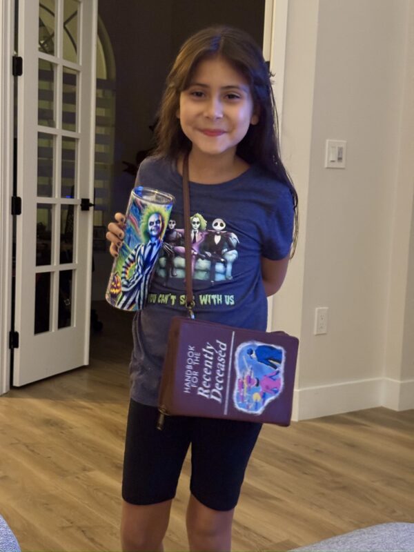 Julie ready to see Beetlejuice 2 with her Neon Beetlejuice tumbler, Beeltjuice and friends tee, and "Handbook for the Recently Deceased" cross body bag (strap is tied up to fit her better)